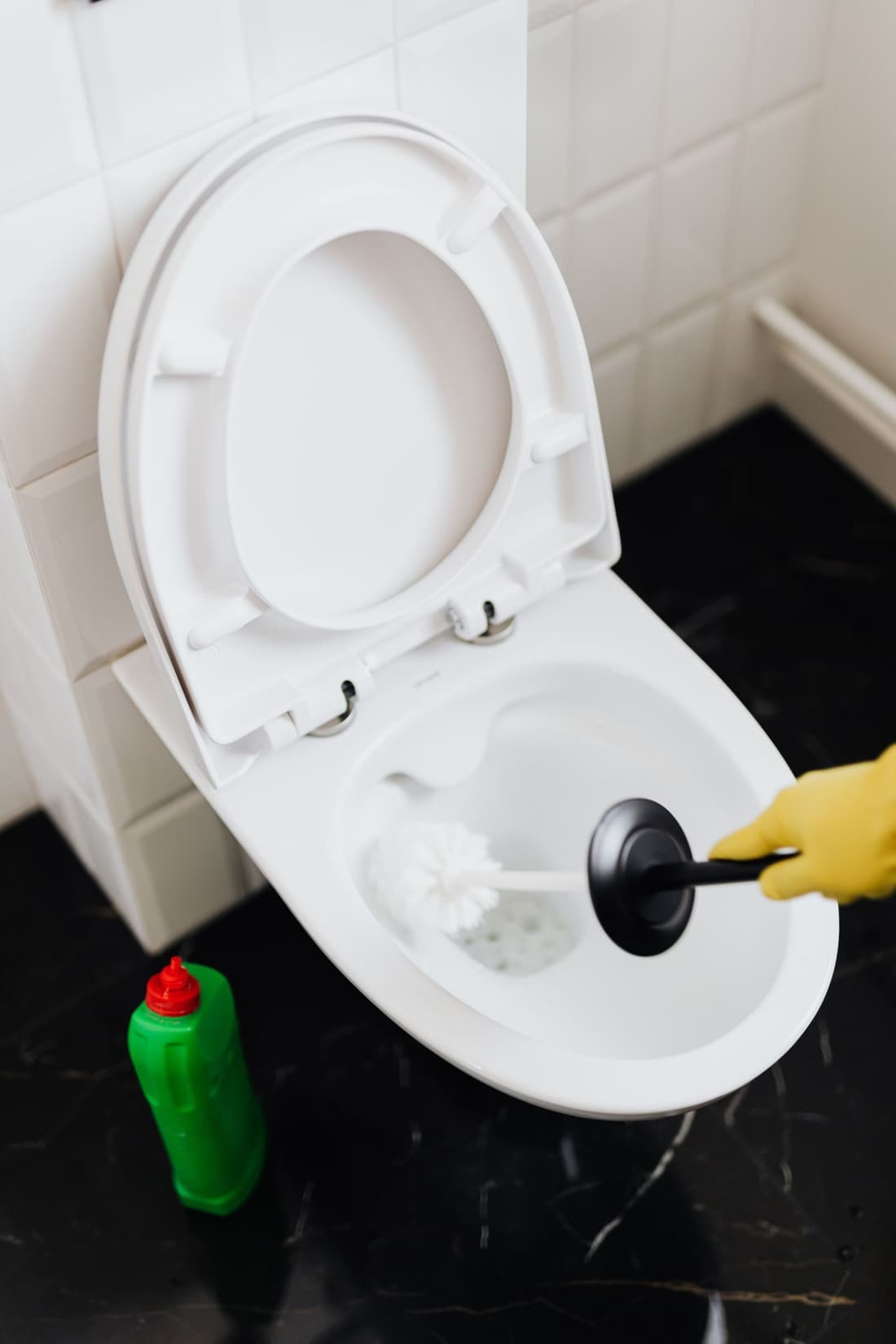 Gloved hand using a plunger to clear a clogged toilet